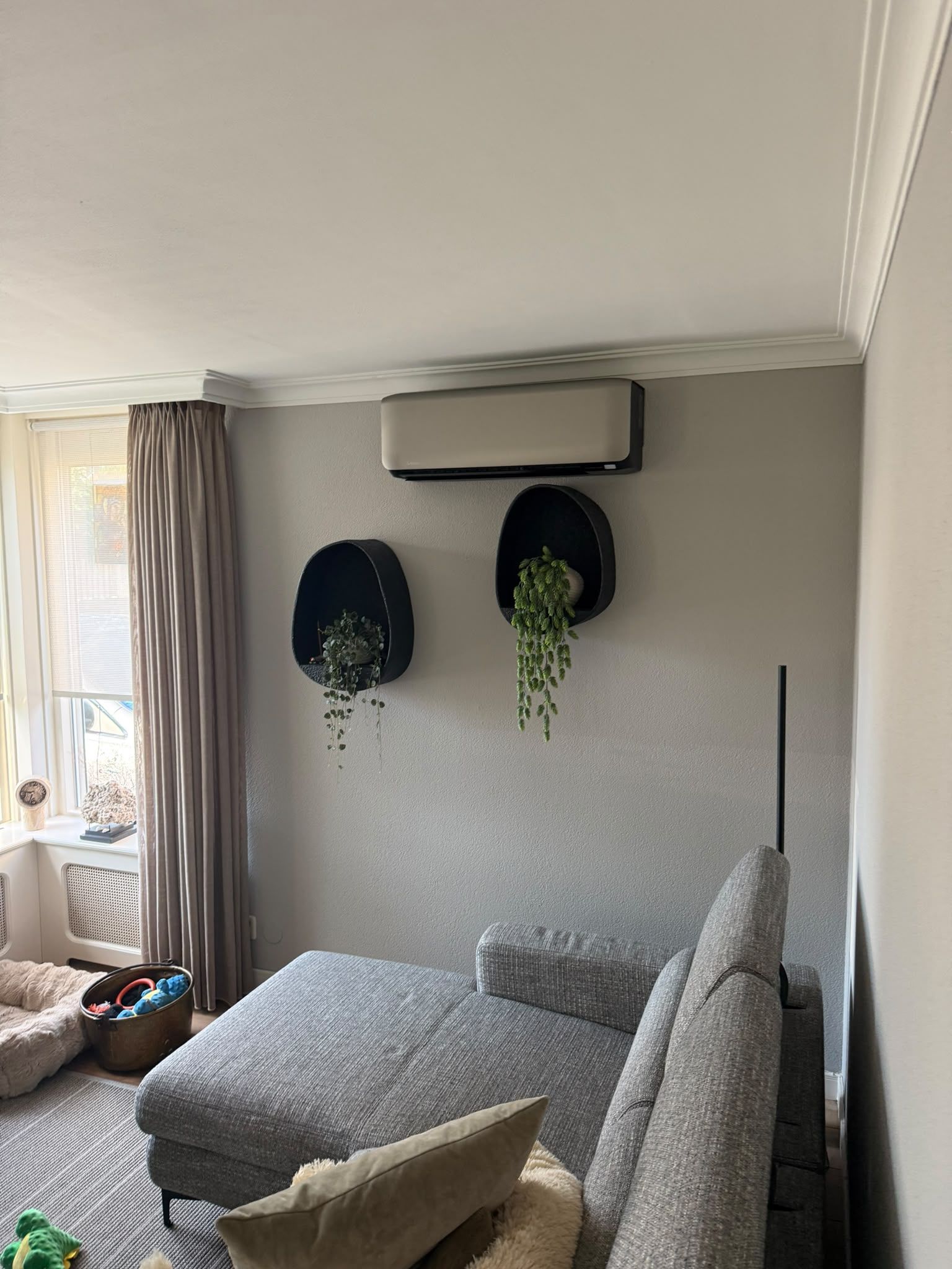 Witte wandunit hoog tegen de muur, boven een grijze loungebank en zwarte wandplanters