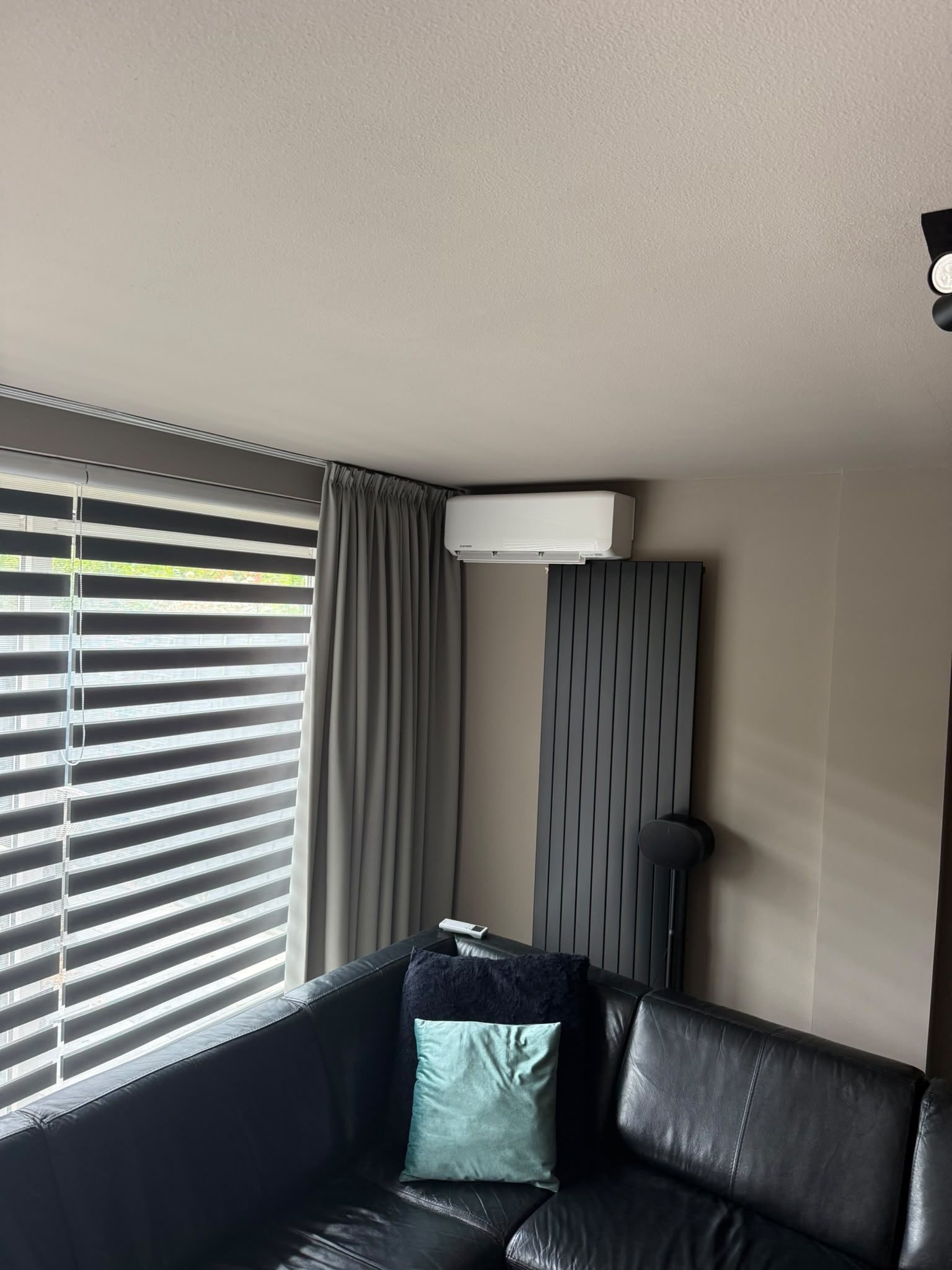 Witte wandunit boven een antraciete designradiator, naast een raam met jaloezieën
