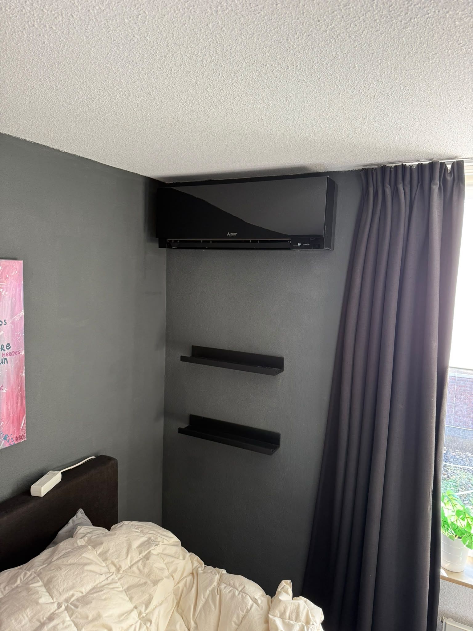 Zwarte wandunit hoog tegen een donkergrijze slaapkamerwand, met twee zwarte wandplankjes eronder