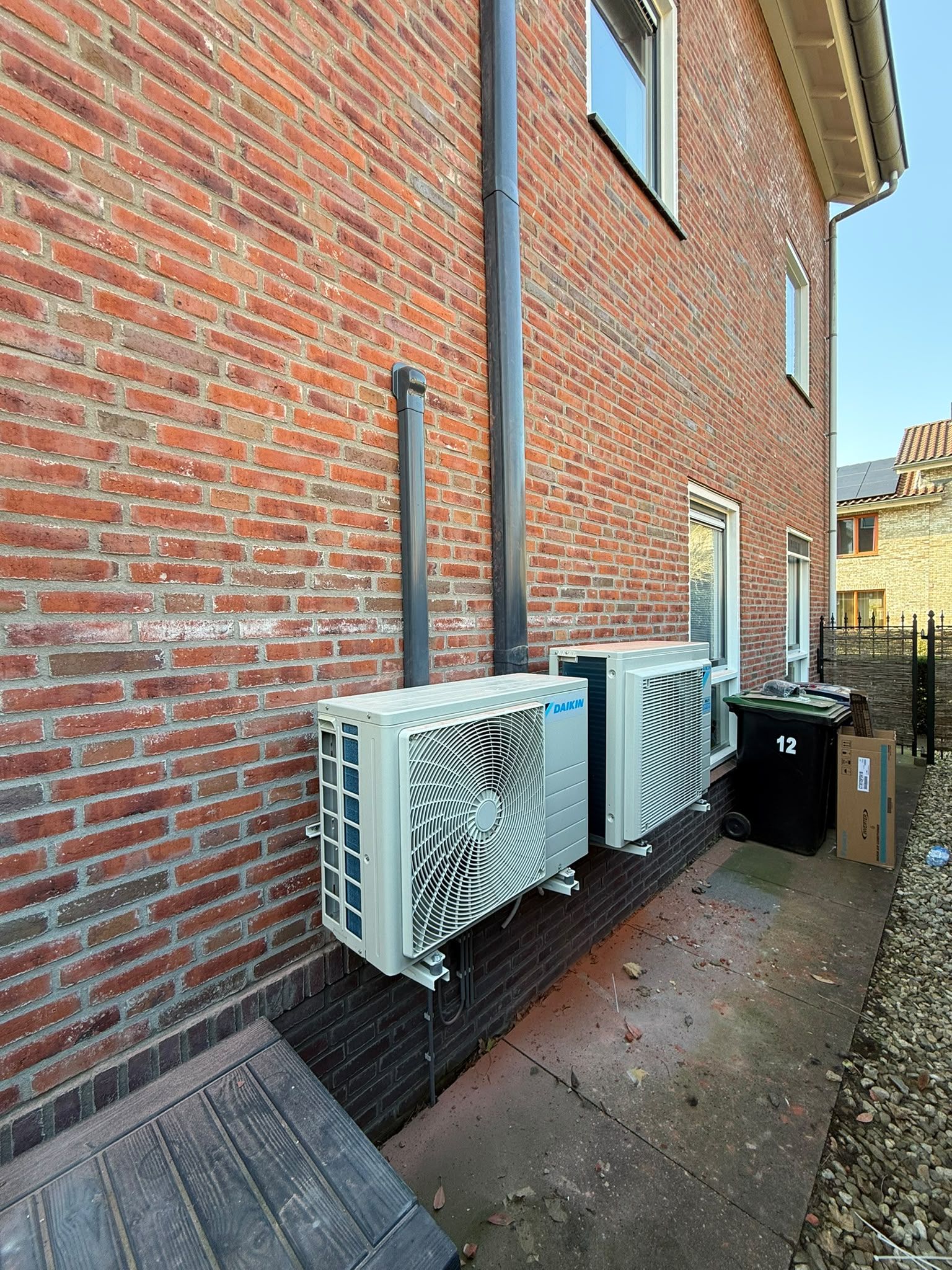 Twee witte Daikin-buitenunits tegen een bakstenen muur in een zijpad