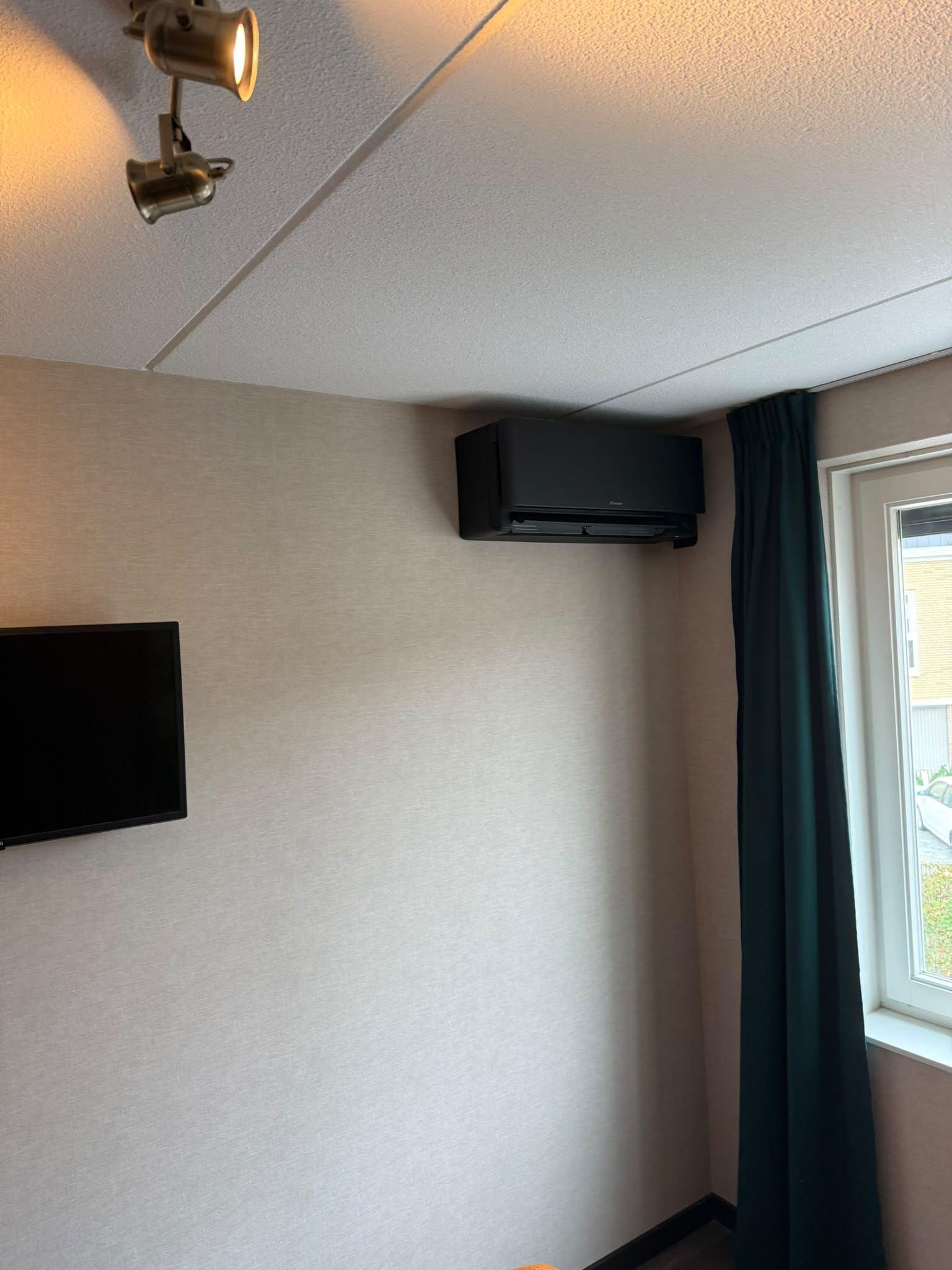 Zwarte wandunit tegen een lichte wand naast een raam met een donkergroen gordijn