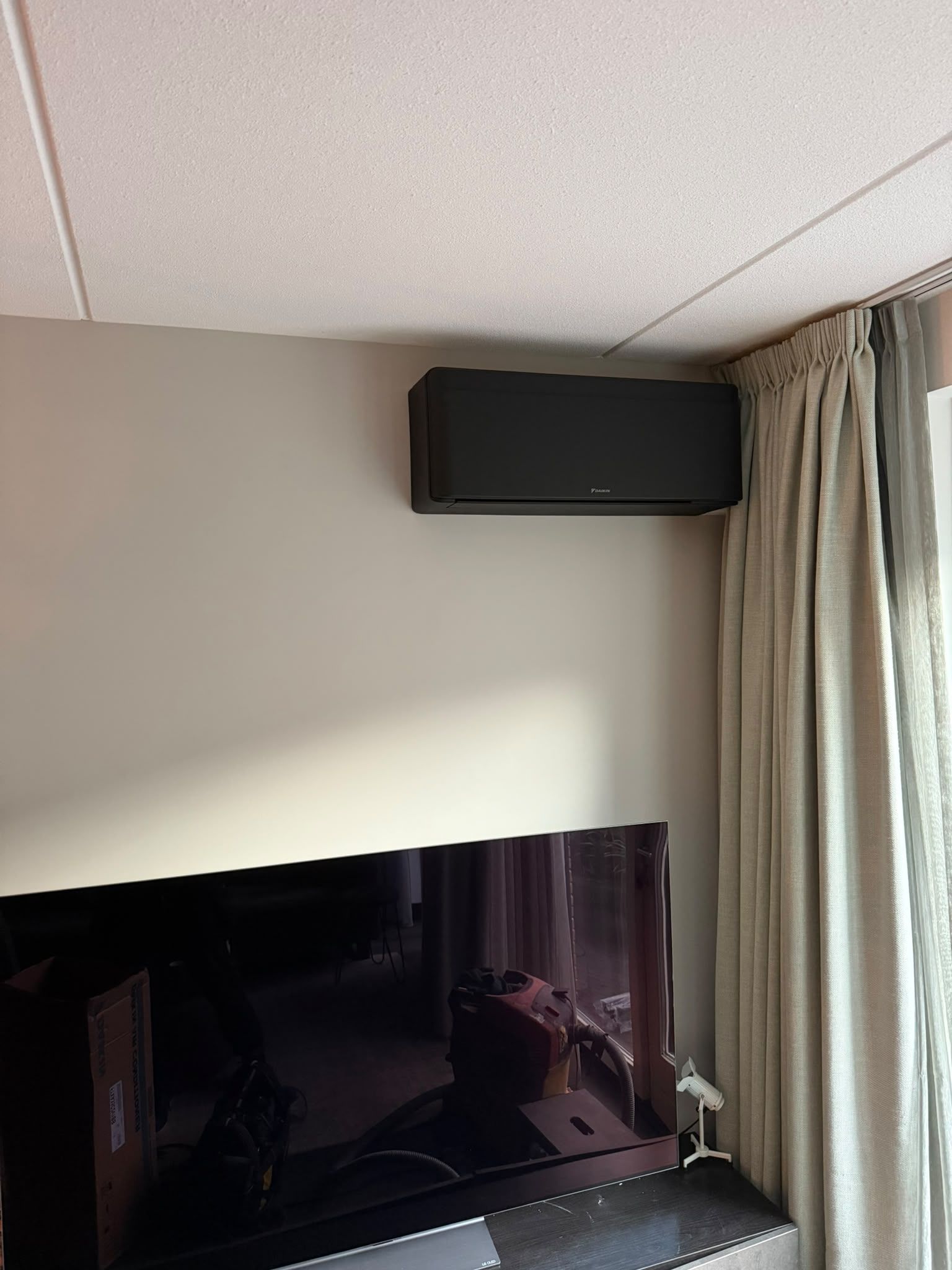 Zwarte wandunit boven een televisie, naast beige gordijnen