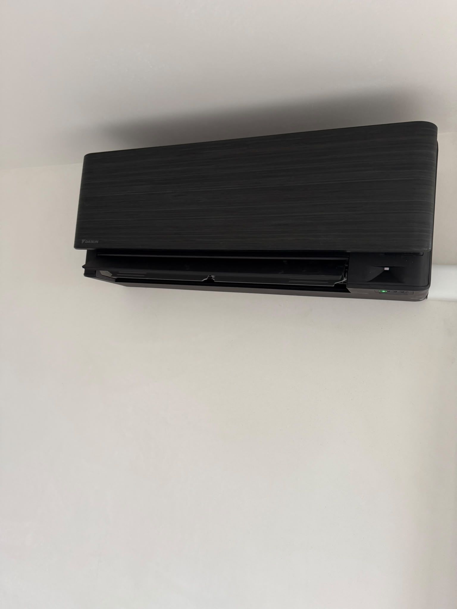 Close-up van een zwarte Daikin-wandunit met houtstructuur tegen een lichte wand