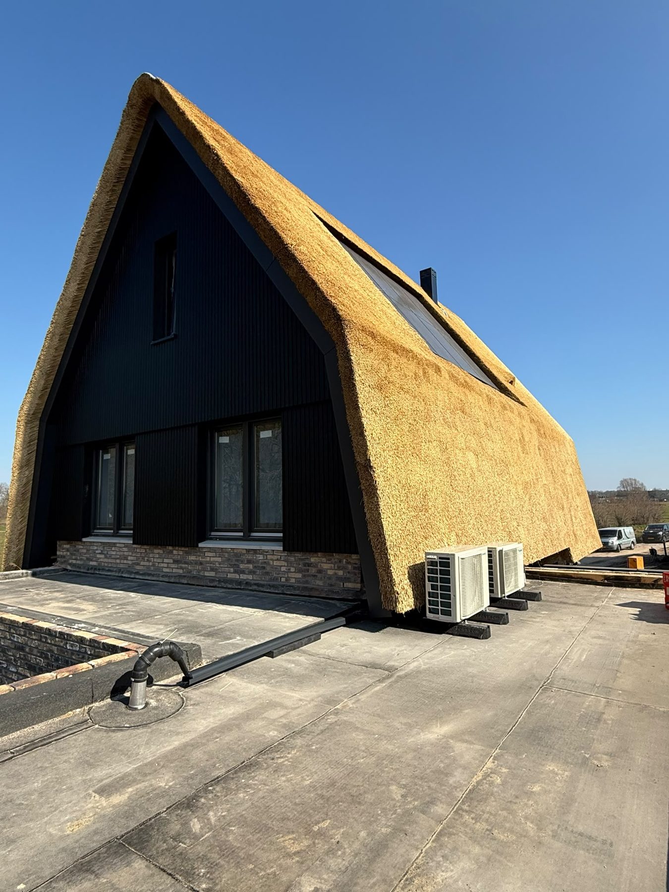 Rietgedekte woning met zwarte gevel en twee buitenunits op het platte dak