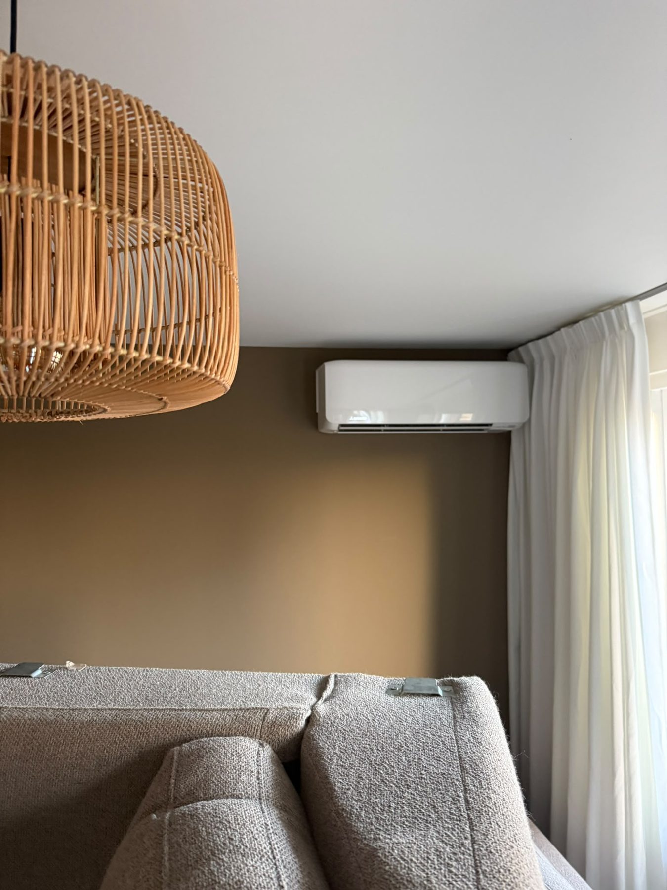Woonkamer met olijfkleurige wand, rotan hanglamp en strak gemonteerde Mitsubishi-airco